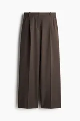 Pantalón sastrero marrón de corte holgado con tiro alto y cierre con corchete y botón ocultos. Piernas amplias con pinzas, pliegues adelante y atrás, bolsillos al bies y bolsillos decorativos atrás.