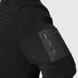 Sweater de punto negro con cuello redondo y manga larga. Presenta un bolsillo con cierre en la manga izquierda.