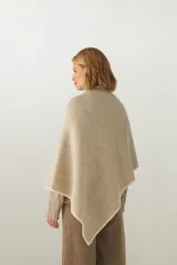 Ruana color crema de tejido de punto industrial con terminación en contraste de color. Tiene doble ojal para mantener el cruce.