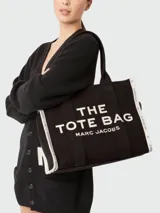 Bolso tote grande Marc Jacobs color beige con estampado del logo de la marca en negro. Tiene doble asa de mano y laterales con inscripción de la marca.