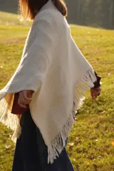 Poncho tejido en lana merino color crudo, con cuello alto y etiqueta de cuero con logo en la espalda.