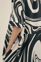 Vestido camisero largo de lino y viscosa con estampado abstracto en blanco y negro. Tiene corte holgado, cuello camisero, mangas cortas, cierre frontal con botones de madera y bolsillos laterales.
