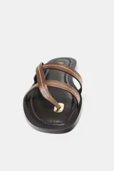 Sandalia plana de piel color marrón con tiras cruzadas en la parte delantera y detalle de pespuntes blancos.