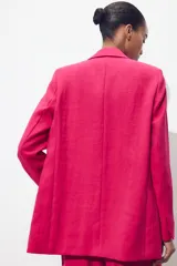 Blazer fucsia de cuello solapa y manga larga con hombreras. Detalle de tejido efecto arrugado. Bolsillos delanteros de vivo. Cierre frontal con un botón.