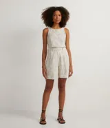 Bermuda corta color beige con estampado floral bordado, de corte sastrero, con bolsillos frontales, cierre por cremallera y botón de presión.