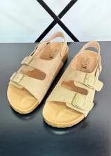 Sandalias planas color marrón claro con dos tiras anchas con hebillas y tira trasera.