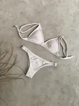 Conjunto de bikini blanco con textura, compuesto por un corpiño de triángulo fijo con breteles regulables y almohadillas desmontables, y una bombacha vedetina con frunce elástico en los costados.