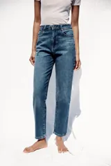 Pantalón de jean gris oscuro, de corte mom fit, tiro alto y largo tobillero. Cuenta con cinco bolsillos, cierre frontal con cremallera y botón.