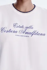 Camiseta blanca de algodón con cuello redondo y detalle de tricot a contraste en azul marino. Estampado frontal con texto "Estate sulla Costiera Amalfitana" en azul marino.