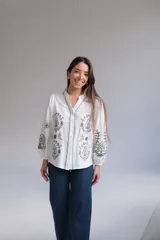 Camisa blanca de manga larga con elástico en puños, cuello mao con botones en la parte delantera y bordados florales en verde.