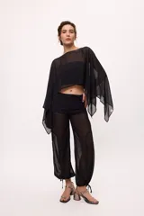 Pantalón negro traslúcido con corte ancho y ajuste en los tobillos.