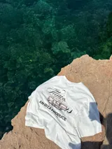 Remera amarilla con estampado en la espalda de una camioneta con una chica y una tabla de surf.