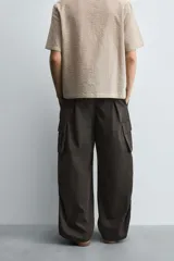 Pantalón cargo de corte ancho y relajado, color verde oscuro o negro, con cintura elástica, bolsillos laterales de parche y bolsillos traseros de vivo. Presenta pliegues verticales marcados en la parte delantera y cordones ajustables en los bajos.