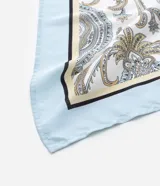Pañuelo rectangular de satén con estampado paisley en tonos blanco, azul claro y beige. El pañuelo se anuda bajo la barbilla, cubriendo la cabeza.