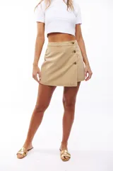 Falda short color beige con diseño cruzado y botones decorativos.