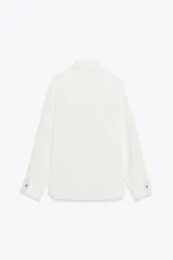 Camisa blanca de satén con cuello solapa y manga larga. Cierre frontal con botones dorados.