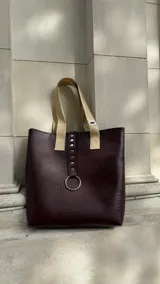 Bolso tote color borgoña con textura símil cuero de cocodrilo y asas color beige. Tiene un aro metálico decorativo, cierre superior y un bolsillo interno.