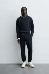 Pantalón jogger negro de corte slim fit, confeccionado en tejido de algodón con cintura elástica ajustable con cordón, bolsillos frontales y traseros de vivo, y bajo con puño elástico.