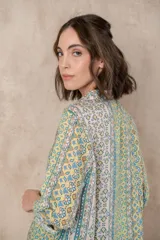 Camisa de manga larga con puños abotonados, cuello clásico y cierre frontal con botones. Presenta un estampado con motivos florales y geométricos en tonos amarillo, verde y celeste.
