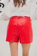 Short de cuerina color rojo, con bolsillos delanteros y traseros, y cierre frontal con botón metálico.
