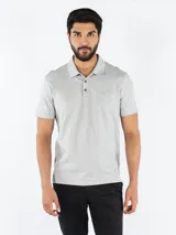 Chomba gris de manga corta, confeccionada en algodón y poliéster, con cuello clásico y tapeta de dos botones. Presenta un monograma de Calvin Klein bordado en el pecho.