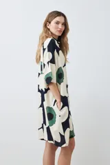 Vestido corto tipo túnica con cuello camisero, manga corta y estampado de margaritas en tonos blanco, verde y azul marino.