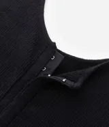 Top cropped sin mangas, color negro, con escote cuadrado y abertura frontal con broches. Presenta textura acanalada.