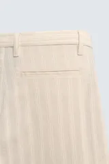 Pantalón chino de corte relajado, color beige claro, con textura de rayas verticales sutiles. Presenta cintura ajustable con cordón interior, bolsillos delanteros y bolsillos traseros de vivo.