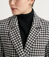 Campera alargada con cuello solapa, bolsillos y cierre de doble abotonado. Presenta un estampado cuadrillé pied-de-poule en blanco y negro, con un detalle contrastante en el puño. Confeccionada en polivelour, con forro de poliéster.