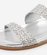 Sandalias planas plateadas con dos tiras trenzadas asimétricas y suela marrón.