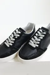 Zapatillas urbanas de cuero negro con cordones negros y suela blanca.
