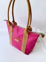 Bolso tipo tote de lona color fucsia con asas de cuero marrón, bolsillo interno y externo.