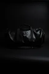 Bolso duffel negro de cuero sintético con logo de ancla bordado en rosa. Tiene doble asa de mano reforzada, correa de hombro regulable y desmontable, cierre superior con doble cremallera y tres bolsillos (dos exteriores y uno interior).