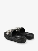 Sandalia tipo plataforma color negro con base de acabado trenzado y capellada ancha decorada con apliques de diseño floral.