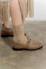 Mocasín de cuero color marrón con tachas metálicas plateadas en la puntera y laterales.