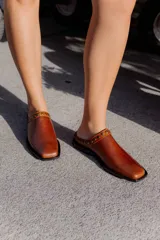 Mules de cuero negro con punta cuadrada y detalle de tachas plateadas en el borde superior.