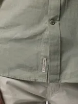 Camisa de hombre color verde oliva, de manga corta y corte clásico. Confeccionada en lino y poliéster, con cuello abotonado y bolsillo en el pecho.