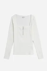 Remera de manga larga color blanco hueso, ajustada al cuerpo, con escote cuadrado y cierre metálico dorado frontal parcial.