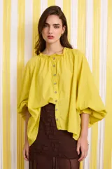 Camisa amarilla holgada de algodón con hombros caídos, mangas anchas, volado en el cuello y botones fucsia.