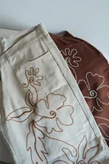 Pantalón slouchy tiro medio color beige con bordado floral marrón.