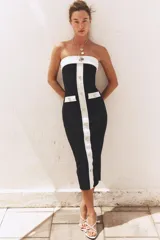 Vestido midi negro de tejido elástico, con escote recto y hombros descubiertos. Presenta falsos bolsillos con botón en el delantero, acabados a contraste en blanco y cierre frontal con botones.