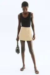 Short pollera color beige de tiro alto con elástico en la cintura, pliegues y botones decorativos en el frente.