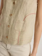 Camisa blanca sin mangas, con cuello camisero, cierre frontal con botones de madera y bolsillo de parche en el pecho.
