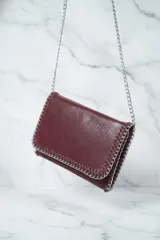 Cartera tipo sobre o clutch negra con textura de cuero envejecido. Presenta bordes decorados con costuras gruesas en contraste y una cadena metálica plateada que sirve como borde y correa de hombro.