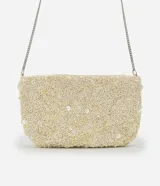 Cartera pequeña transversal color crema, cubierta de lentejuelas y cuentas. Tiene asa de cadena plateada y cierre de cremallera.