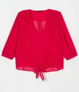 Blusa de crepe color fucsia, con escote en V, mangas 3/4, textura de lunares y amarre en la parte delantera.