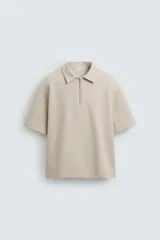 Polo color beige de corte relaxed fit, confeccionado en tejido interlock de algodón con elasticidad. Tiene cuello solapa con cierre frontal de cremallera y manga corta.