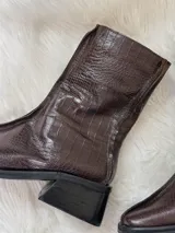 Botas cortas color chocolate con textura de cocodrilo, punta cuadrada y tacón bajo. Cuentan con cierre lateral.