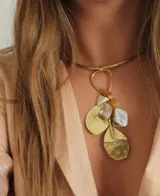 Gargantilla rígida dorada con colgante de piedras irregulares color blanco, naranja y dorado, y dijes de metal dorado en forma de hojas.