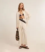 Pantalón recto de cintura alta confeccionado en viscolino color crudo, con elástico en la parte trasera de la cintura, cierre tradicional y textura de palmeras perforadas en el bajo.